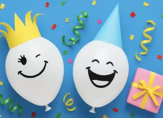 150 Felicitaciones de Cumpleaños Graciosas (2025) Dos globos blancos sonrientes (uno con corona amarilla y otro con gorro azul) junto a confeti y regalo rosa sobre fondo azul