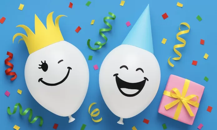 Dos globos blancos sonrientes (uno con corona amarilla y otro con gorro azul) junto a confeti y regalo rosa sobre fondo azul