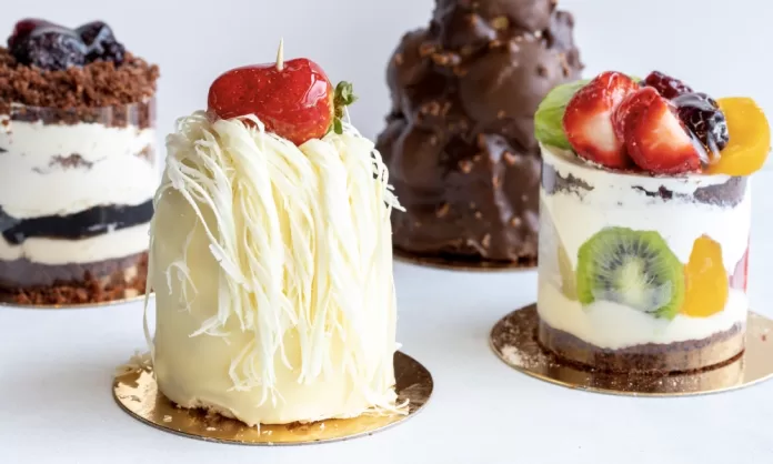 Cuatro postres individuales con chocolate, hebras de chocolate blanco y frutas frescas sobre fondo claro