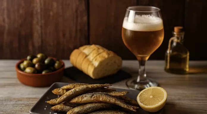 Boquerones: qué son, cómo se preparan y cómo servirlos en fiestas Boquerones fritos con limón servidos como tapa, acompañados de pan, aceitunas, aceite de oliva y cerveza sobre mesa rústica.
