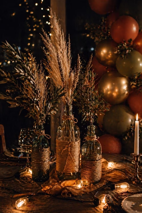 Centro de mesa rústico con botellas de vidrio, ramas secas, velas y globos en tonos cálidos