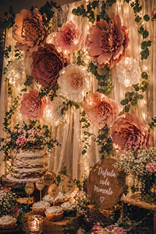 Fondo de cumpleaños con flores gigantes de papel, luces cálidas y mesa dulce decorada