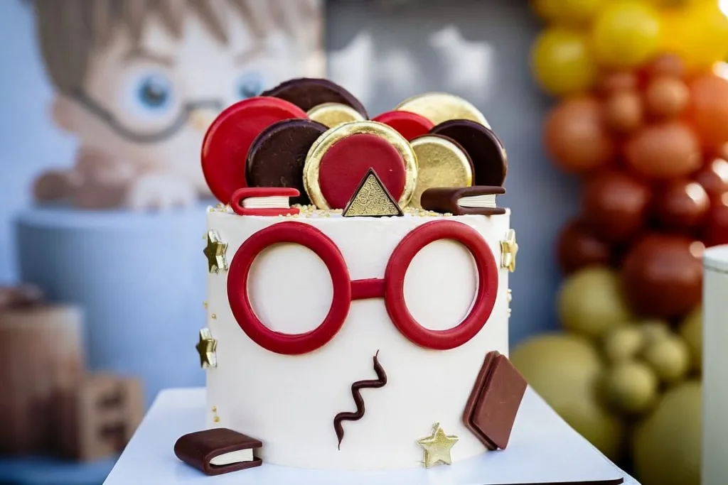 Tarta inspirada en Harry Potter con gafas rojas, cicatriz, libros, estrellas y decoración en rojo, dorado y chocolate.