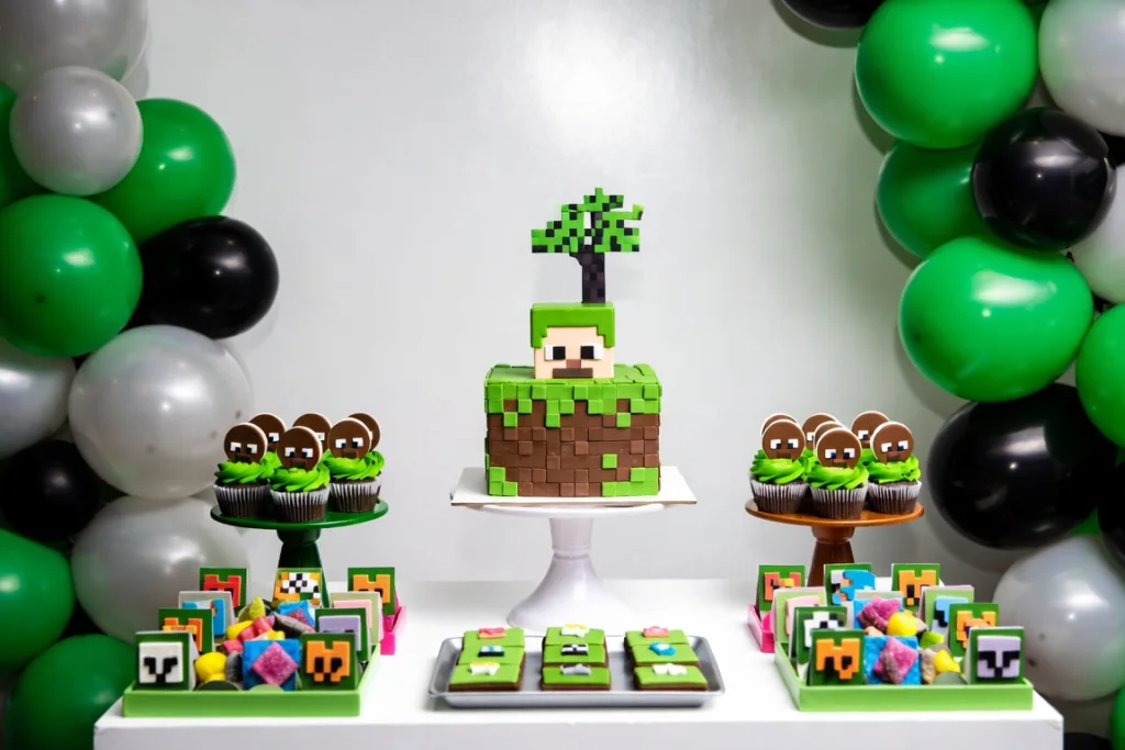Mesa dulce temática con tarta de bloques, cupcakes, dulces de colores y globos verdes y negros