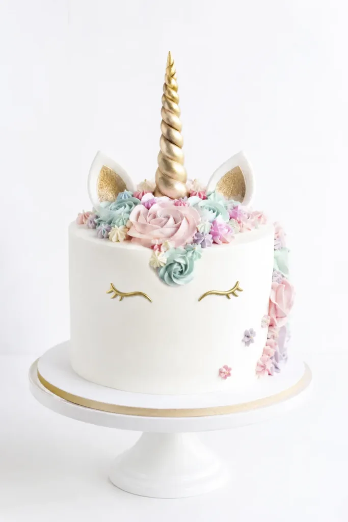 Tarta de cumpleaños infantil con cobertura blanca, flores pastel, cuerno dorado y un diseño moderno.